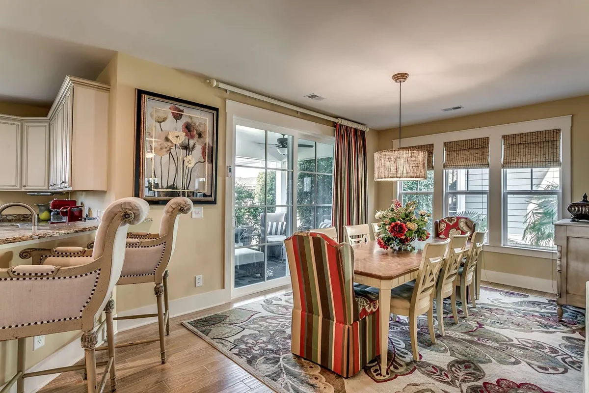 An inviting dining area with a table set for a meal, adorned with a floral centerpiece. Striped dining chairs surround the table, and the space also features a kitchen bar area and framed wall art. The ambiance is warm and sociable, ideal for group dining experiences.