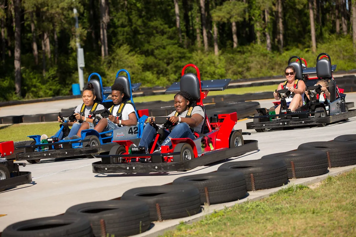 A dynamic go-kart track in action, with smiling participants enjoying thrilling races. The grouping of go-karts and the lively track environment highlight an atmosphere of excitement and playful competition that appeals to various age groups.