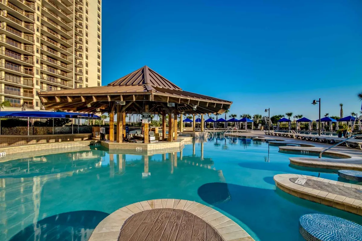 An inviting outdoor pool area featuring a sparkling pool surrounded by comfortable sun loungers and a cozy cabana. The sky above is bright and clear, and the setting suggests a place for relaxation, swimming, and family gatherings.