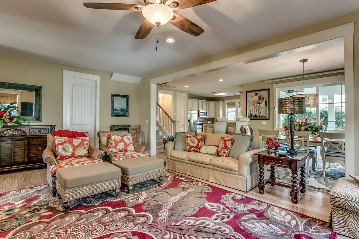 The image showcases a bright, inviting living area with a colorful floral rug anchoring cozy, plush seating. Tasteful wall art and a decorative lamp add character and warmth to the space, which feels perfect for gathering, relaxing, and making memories with family or friends.