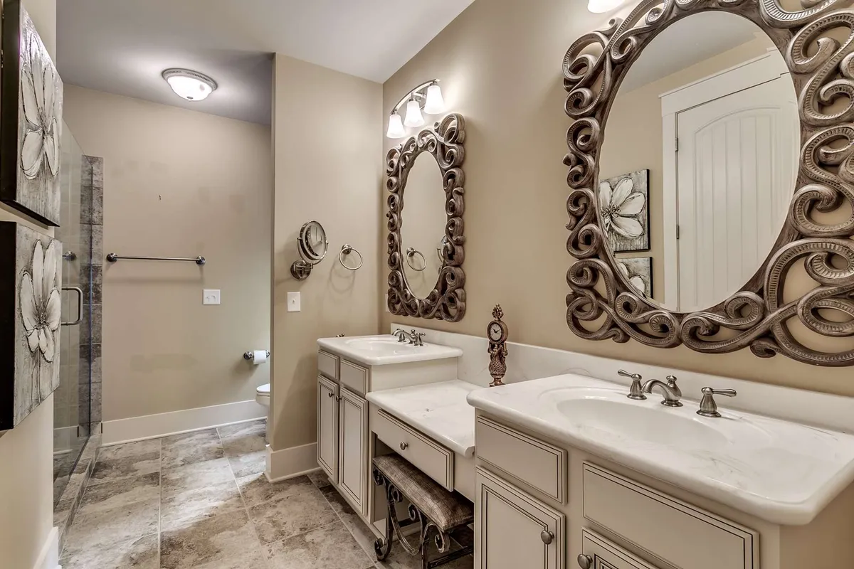 A luxurious bathroom featuring a double vanity with ornate mirrors and a spacious walk-in shower. Decorative wall art adds an elegant touch. The space is both functional and sophisticated, perfect for morning routines or relaxing after a busy day.