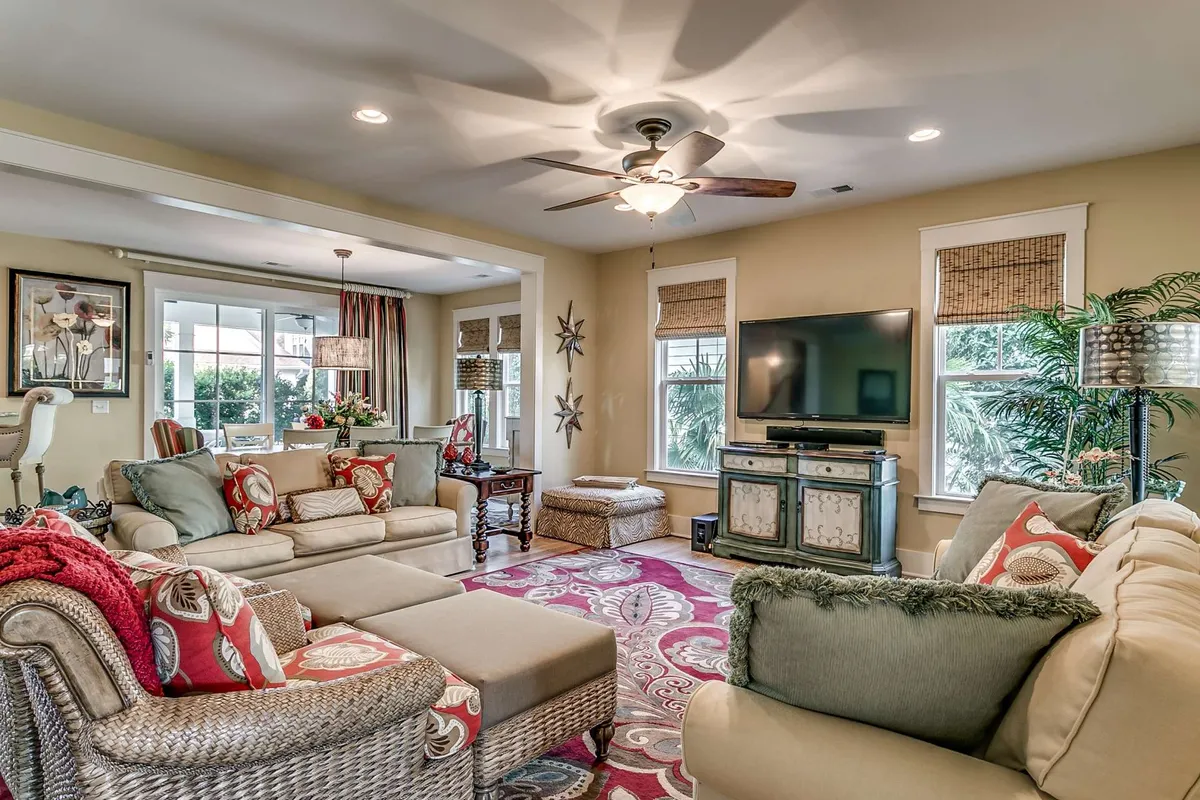 A spacious living room featuring a large sectional sofa atop a colorful area rug, complemented by a media console and decorative wall art. The setting is bright and inviting, with plenty of seating for groups to gather, relax, or watch movies together.