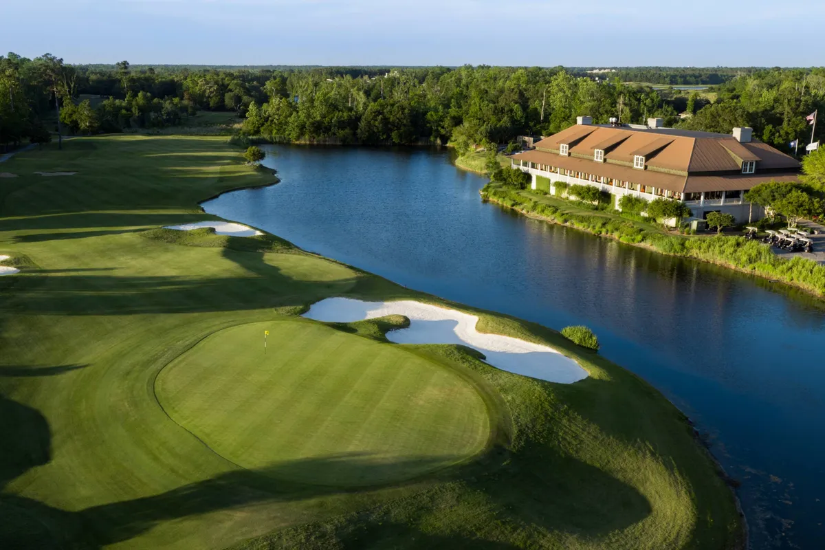 A scenic view of the Azalea Sands Golf Club, featuring manicured greens, a tranquil water body, the clubhouse in the background, and sand traps dotting the landscape. The scene is bathed in warm light, evoking a relaxing atmosphere ideal for golfers and leisure seekers.