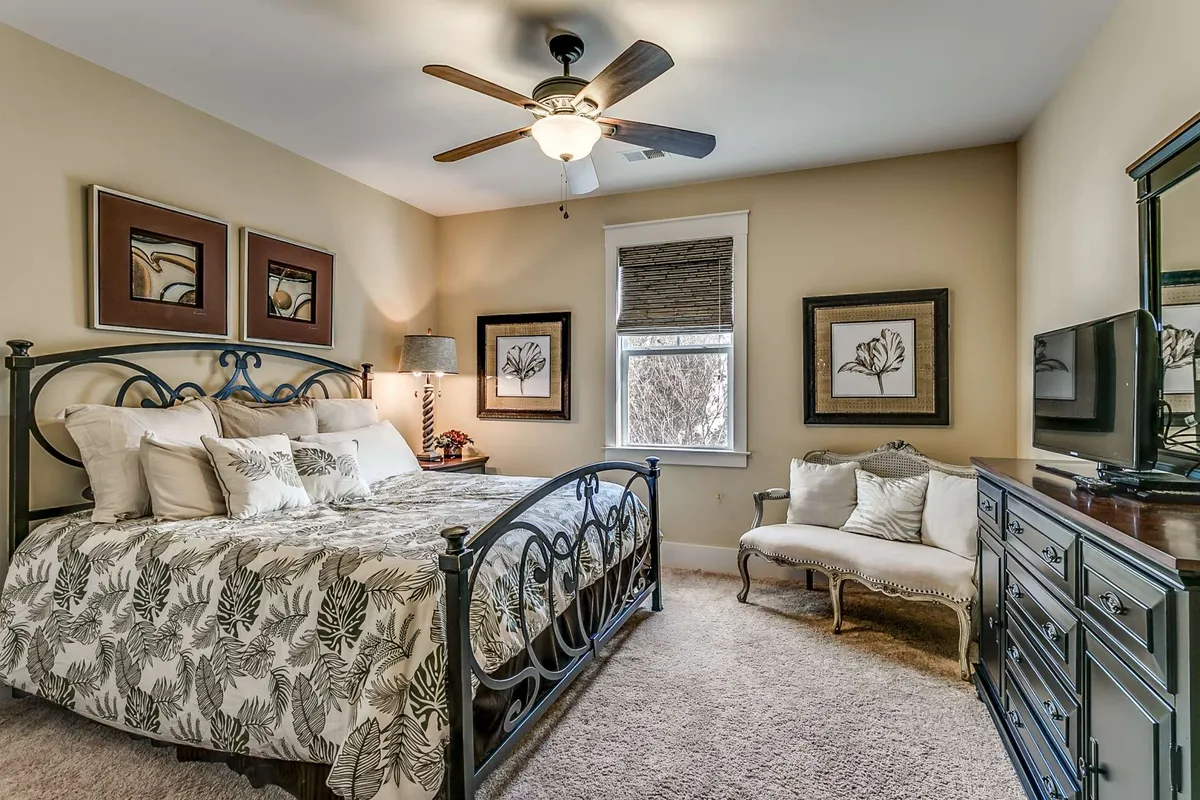 A cozy bedroom with a bed dressed in floral bedding, a plush armchair and ottoman for reading or relaxing, a dresser with a mirror, and tasteful wall art. The ambient light and soothing decor create a haven for rest and quiet moments.