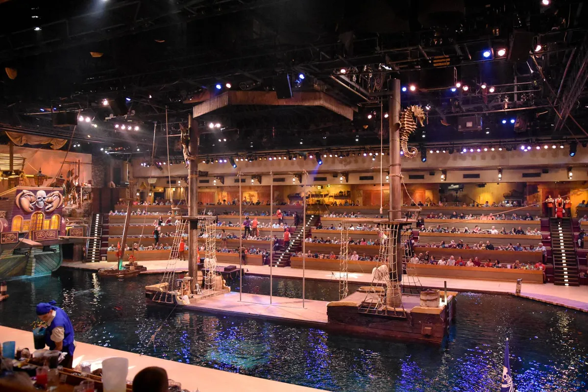 A dynamic interior setting with a water stage, pirate ship set, audience seating, and performance area, hinting at lively entertainment and immersive experiences offered at the resort or nearby attractions.